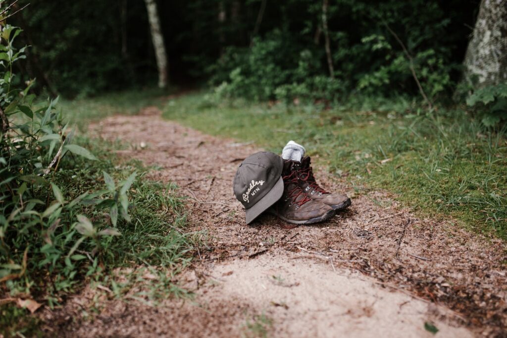 a pair of brown hiking boots along a dirt road below trees beside a dried mud puddle