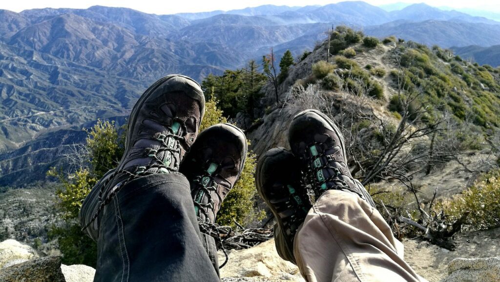 Shoes for outdoor activities worn by two people staring at the horizon and green mountains.