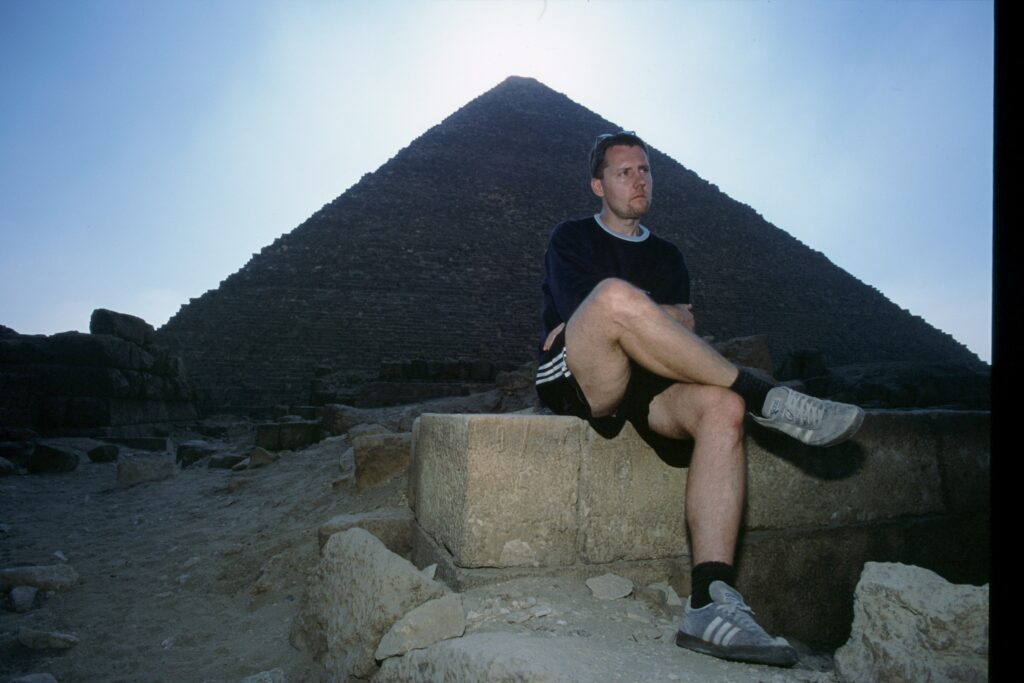 Man wearing shoes for outdoor activities posing for a picture in front of the Egyptian pyramids.